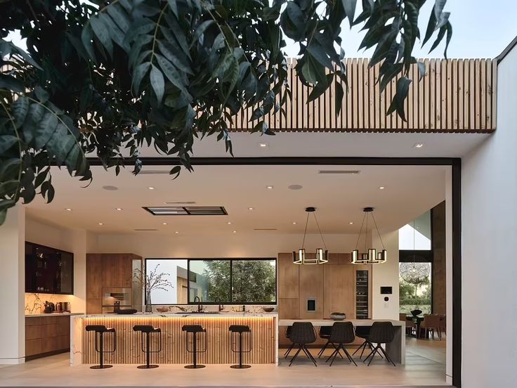 an open kitchen and dining area with bar stools in the foreground, surrounded by greenery