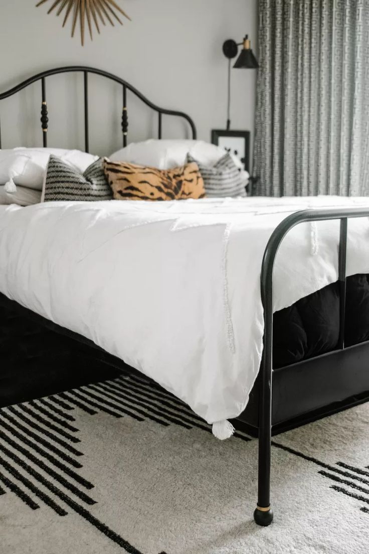 a black metal bed frame with white sheets and pillows on top of it in a bedroom