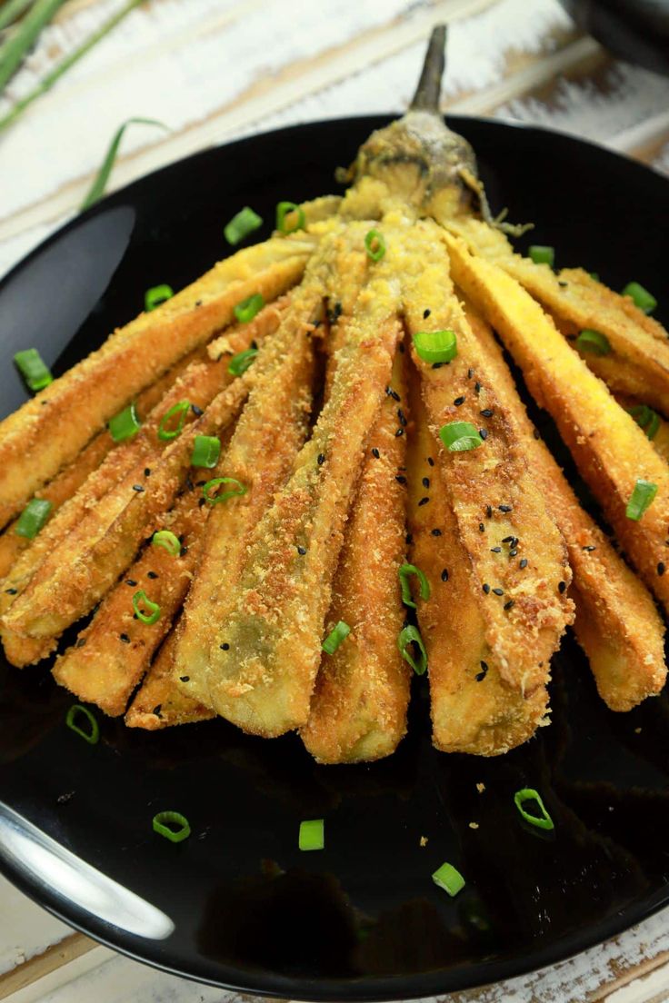 some fried food on a black plate with green onions and seasoning sprinkles