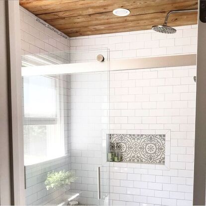 a white tiled bathroom with wooden ceiling and window