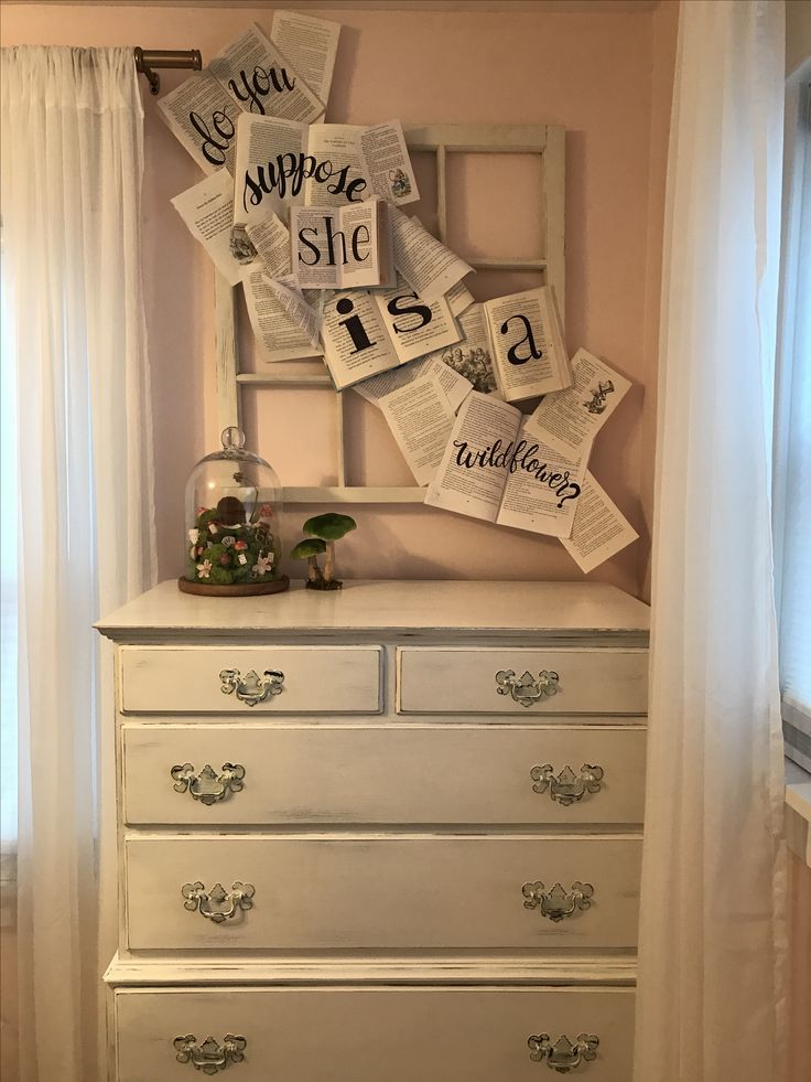 a white dresser with pictures on it and some papers hanging from the wall above it