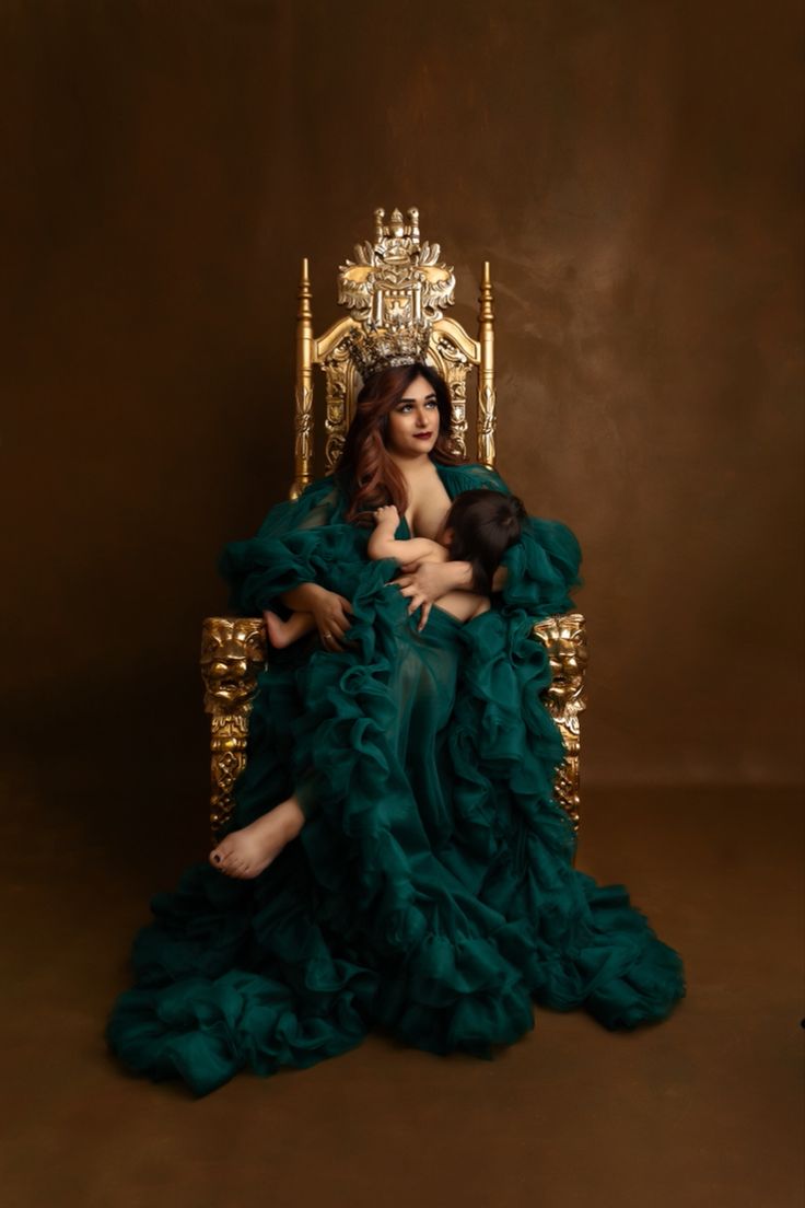 a woman in a green dress sitting on a golden throne with her baby wrapped around her