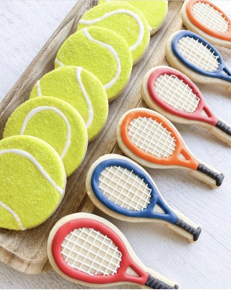 cookies decorated like tennis rackets and balls on a wooden platter with white background