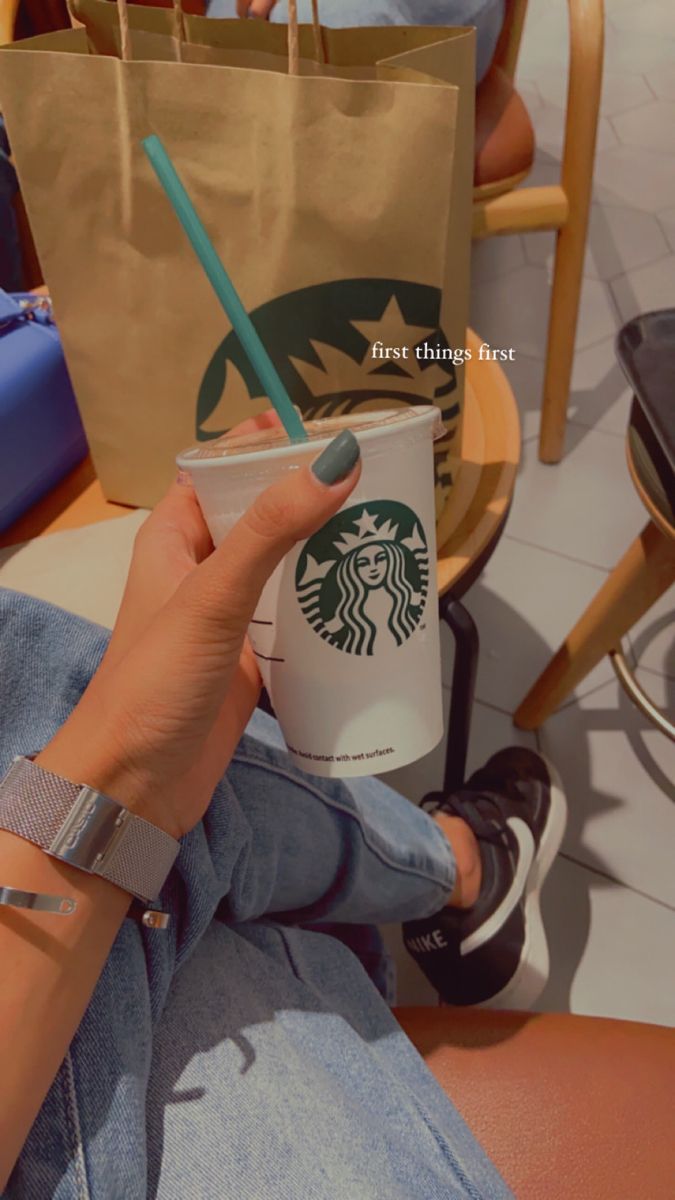 a woman holding a starbucks cup with a straw in it's hand while sitting on a chair