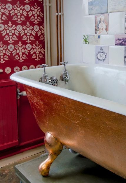 an old fashioned bathtub in a bathroom with red cabinets and pictures on the wall