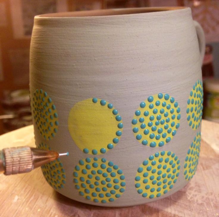 a vase with yellow and blue dots on it sitting on top of a wooden table