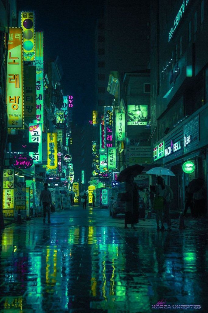 a city street at night with neon signs on the buildings and people walking in the rain