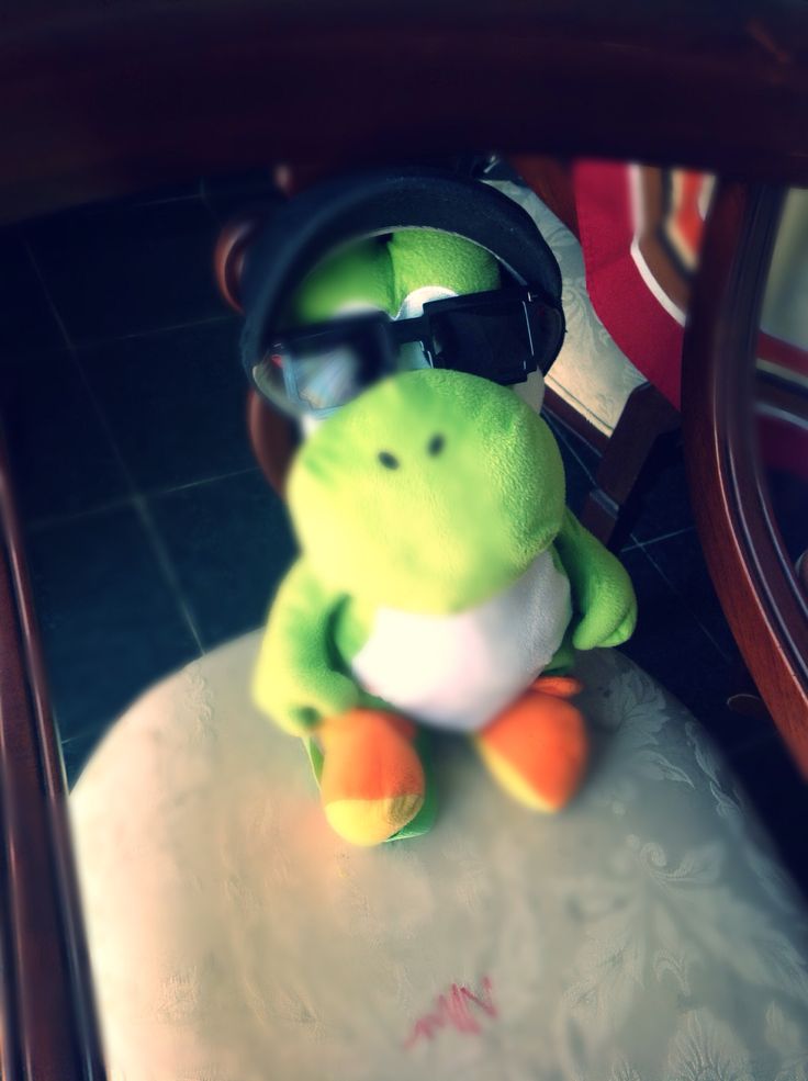 a green stuffed animal with goggles and a hat sitting on top of a table