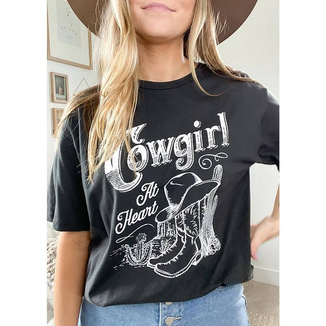 Womens Cowgirl At Heart Print T Shirt Fitted Graphic Print T-shirt For Rodeo, Trendy Relaxed Fit T-shirt For Rodeo, Western Style Cotton T-shirt For Rodeo, Spring Letter Print T-shirt For Rodeo, Black Top For Spring Rodeo, Graphic Print T-shirt For Rodeo, Western Style Cotton Tops With Screen Print, Western Style Cotton Graphic T-shirt, Cotton Graphic Tee Tops For Rodeo