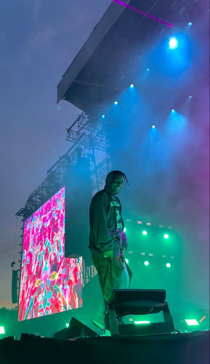 a man standing on top of a stage next to a large screen with colorful lights