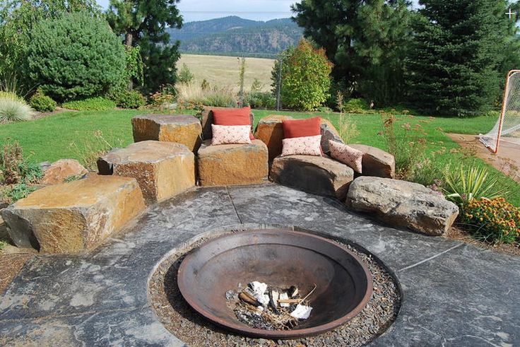 an outdoor fire pit surrounded by rocks and pillows