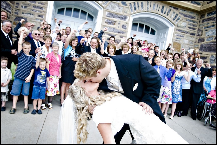 a bride and groom kissing in front of a large group of people