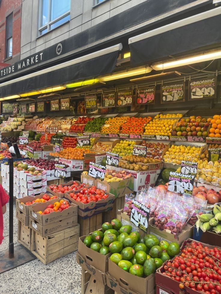 a woman standing in front of a produce stand with lots of fruits and vegetables on display