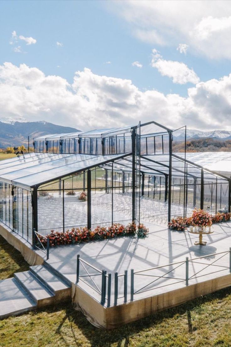 a glass house sitting on top of a lush green field next to a lake and mountains