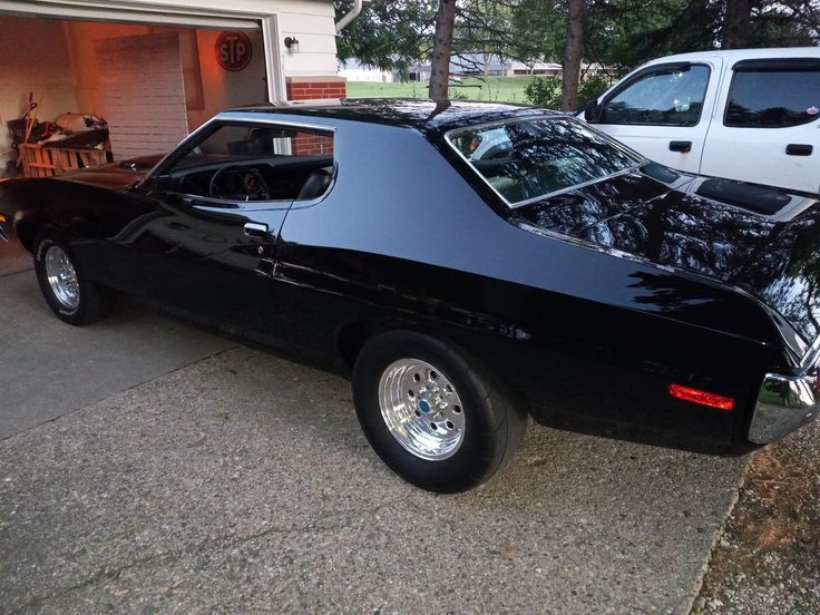 a black muscle car parked in front of a garage