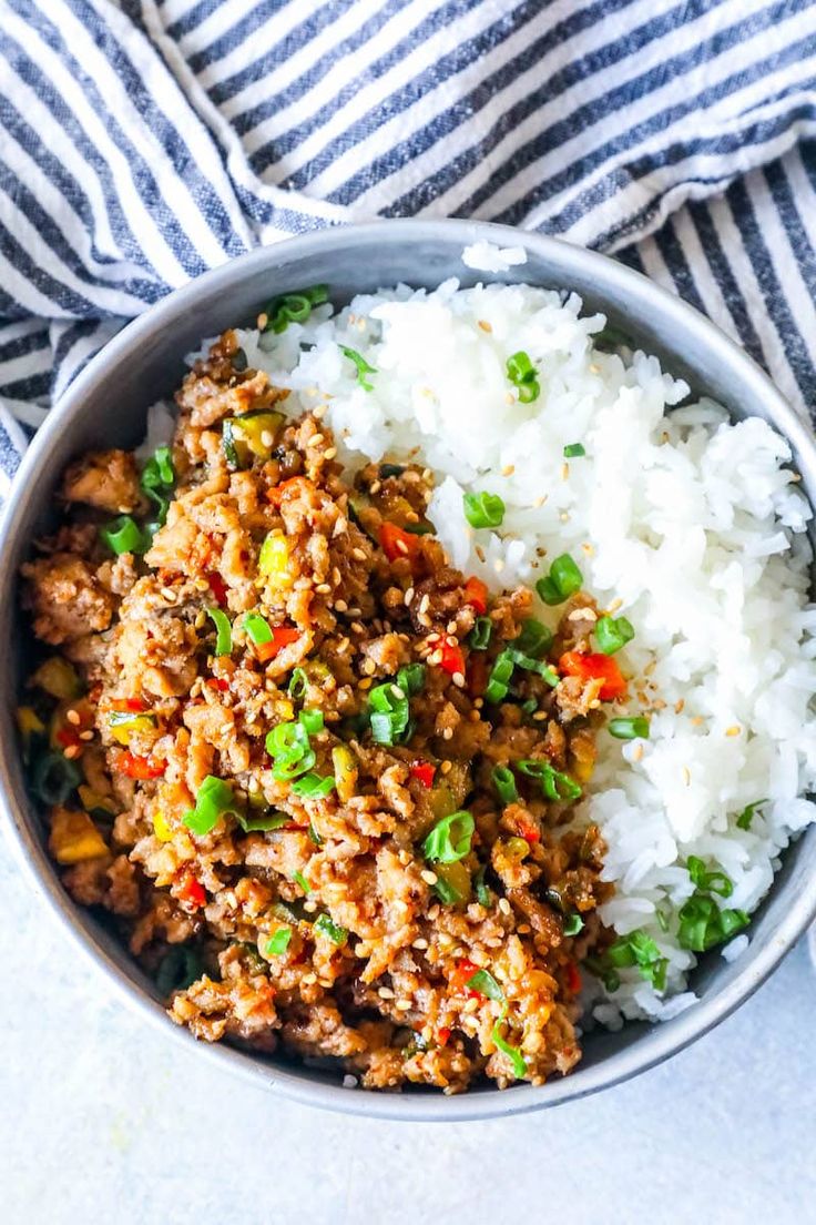 a bowl filled with rice and meat on top of a striped cloth next to a fork