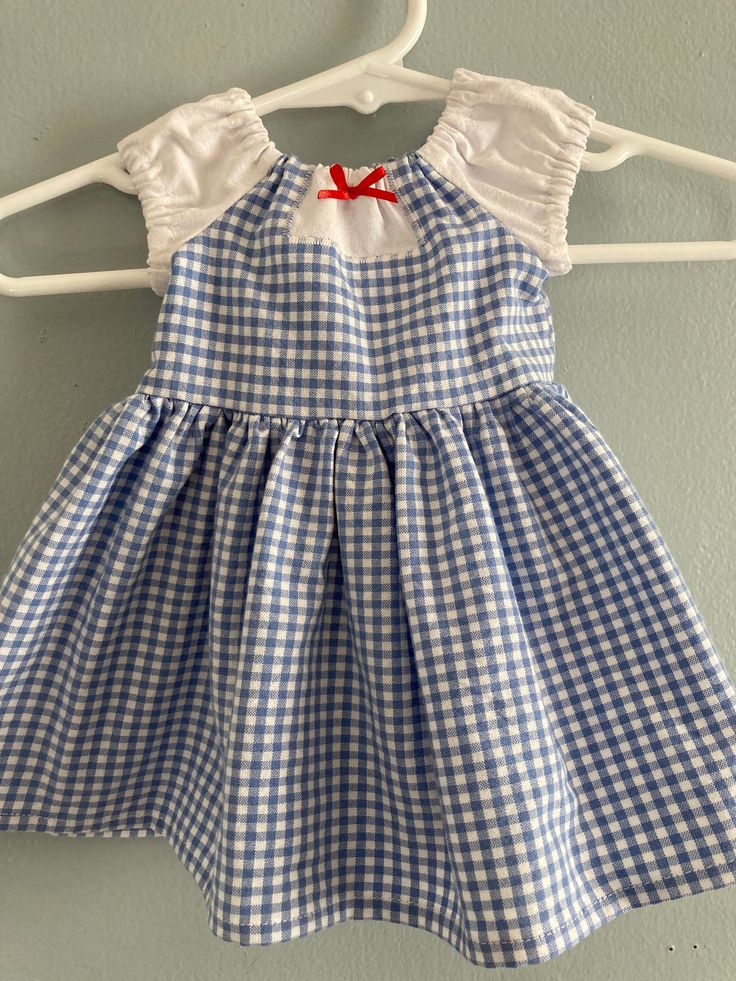 a blue and white gingham dress hanging on a hanger with a red bow