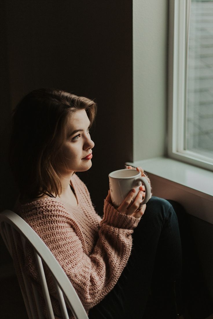 a woman sitting on a chair holding a cup in her hand and looking out the window