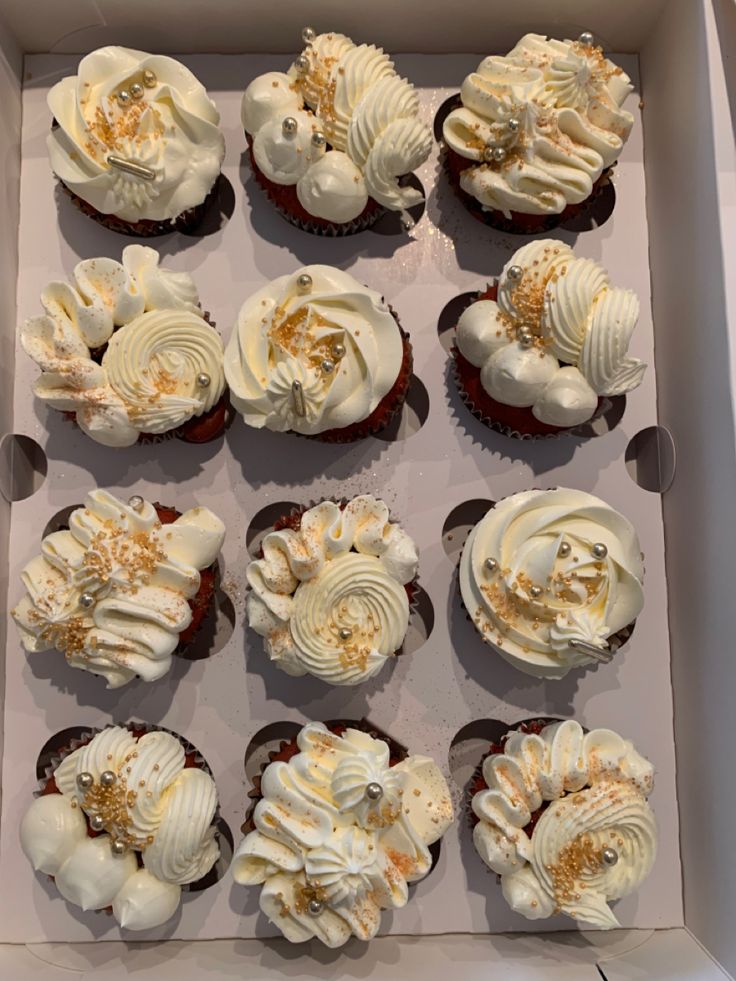 twelve cupcakes with white frosting and sprinkles in a box