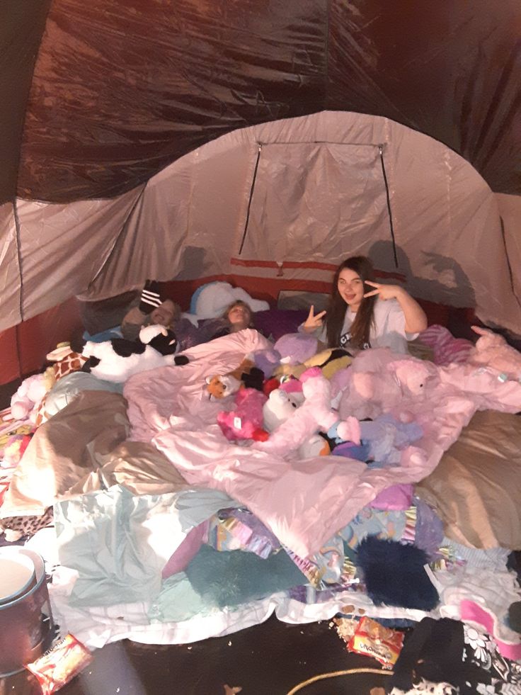 two women laying in a tent with stuffed animals on the bed and other items scattered around