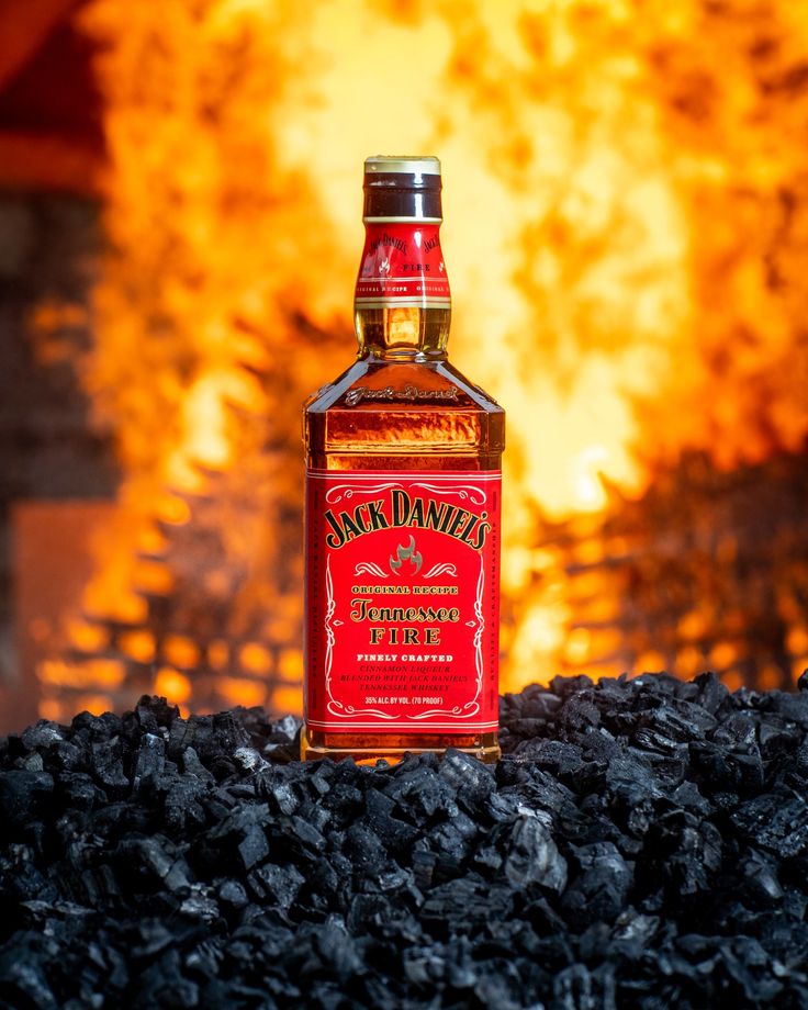 a bottle of jack daniels whiskey sitting on top of black coal in front of a fire