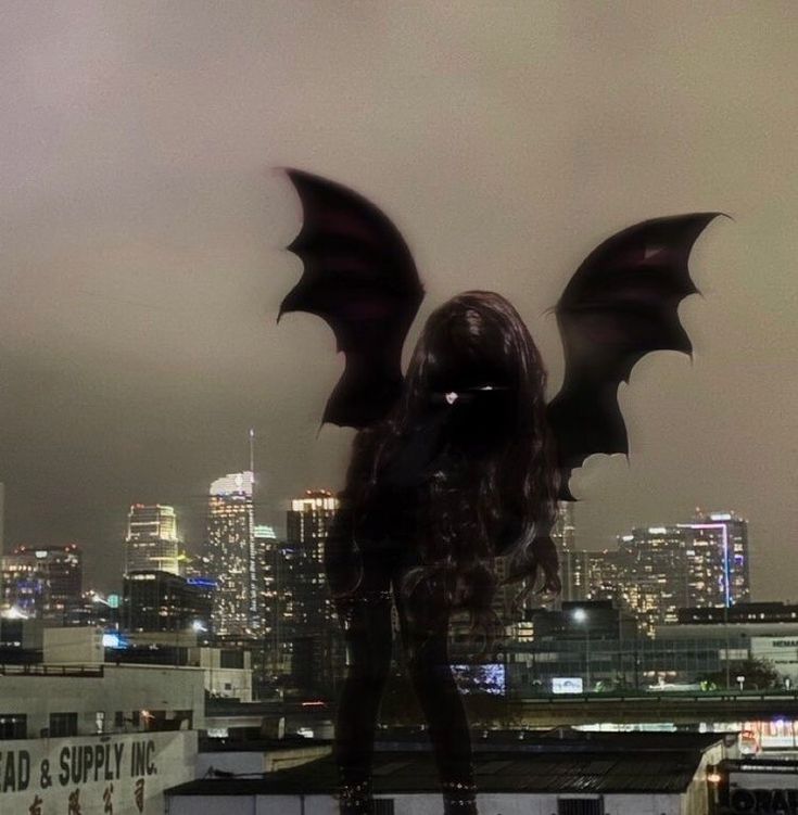 a woman standing on top of a roof next to a tall building with large wings