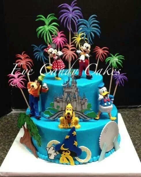 a blue cake with mickey mouse figures on top and palm trees in the back ground