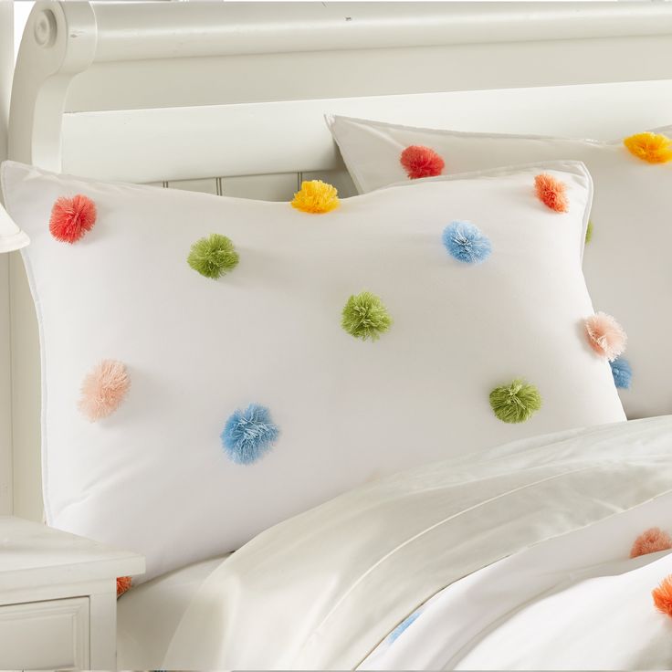 a white bed topped with pillows and colorful pom poms