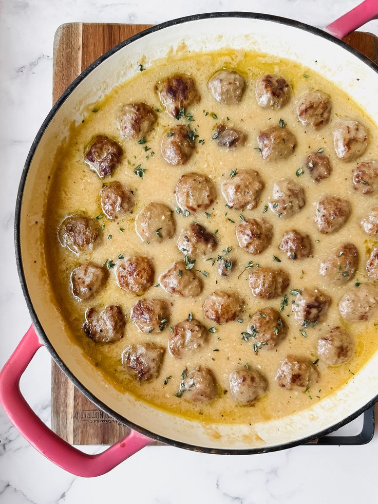 a pan filled with meatballs and gravy on top of a wooden cutting board