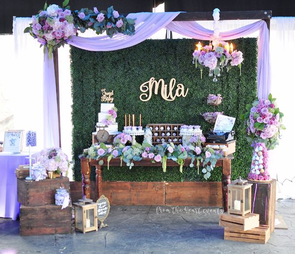 a table topped with lots of purple flowers next to a wall covered in greenery