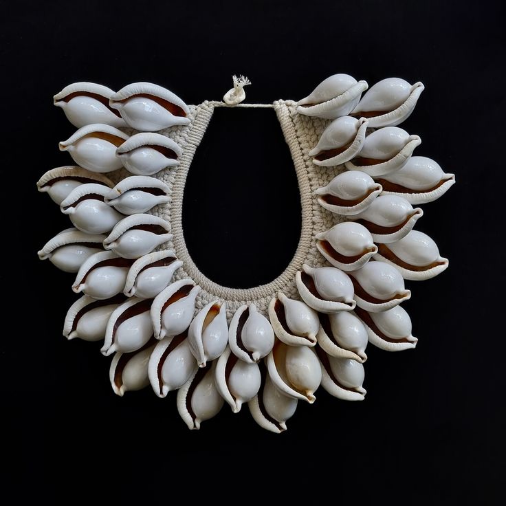 Elevate your style with the White Ovula Ovum (White Egg Cowrie) Shell Necklace, a captivating piece of tribal fashion hailing from the rich traditions of Papua New Guinea. This exquisite necklace is more than just an accessory; it's a wearable work of art that seamlessly marries cultural heritage with contemporary women's fashion. Each meticulously selected Ovula shell in this necklace reflects the timeless craftsmanship of Papua New Guinean artisans. The soft, iridescent white shells, delicatel Unique White Shell Pendant Necklace, Unique White Pendant Shell Necklace, Traditional White Fair Trade Necklaces, Traditional Handwoven Natural Jewelry, Traditional Handwoven Natural Color Jewelry, Traditional White Fair Trade Necklace, Traditional Shell Necklace Gift, Elegant Handwoven Natural Jewelry, Elegant Handwoven Jewelry