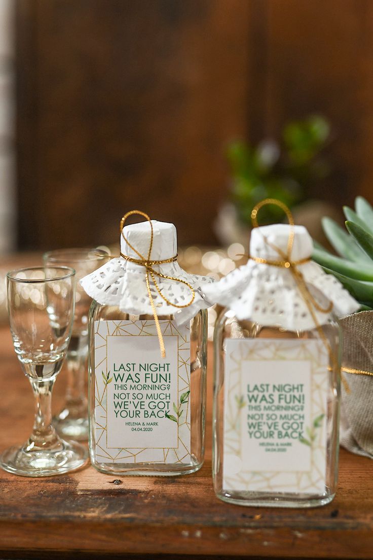 two glass jars with labels on them sitting on a table next to wine glasses and succulents