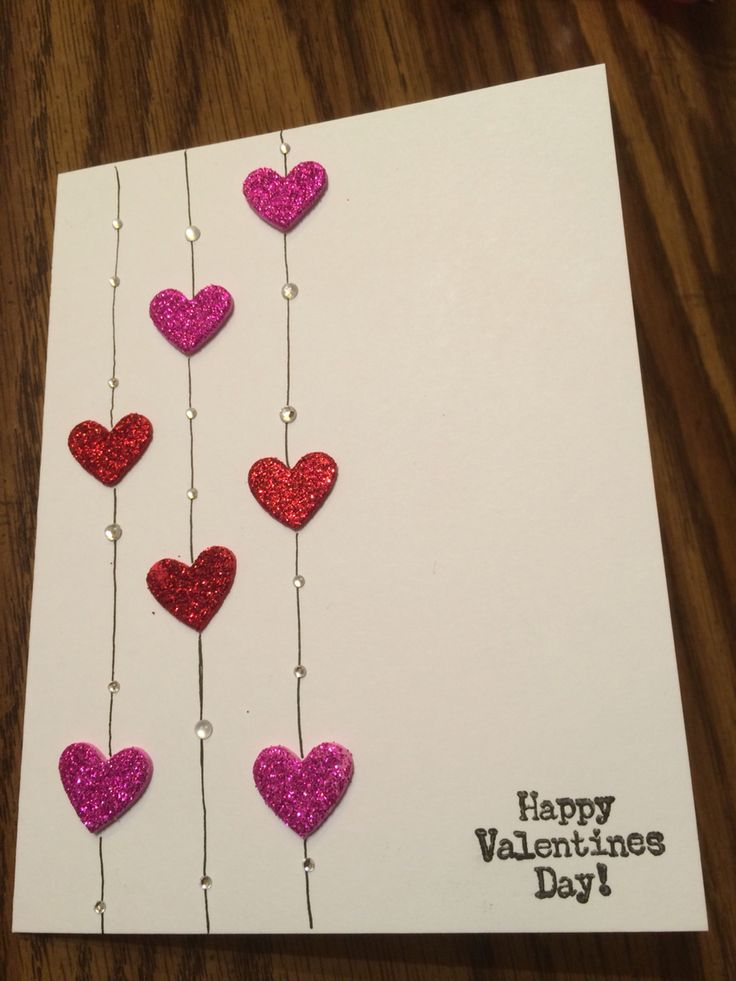 valentine's day card with pink and red glitter hearts hanging from strings on white paper