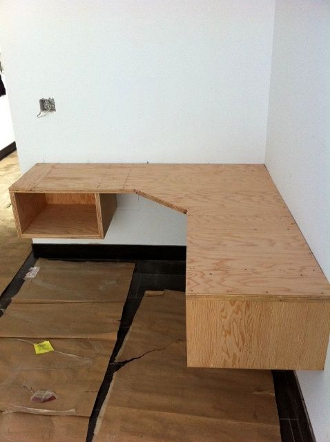 a wooden desk sitting on top of a hard wood floor next to a white wall