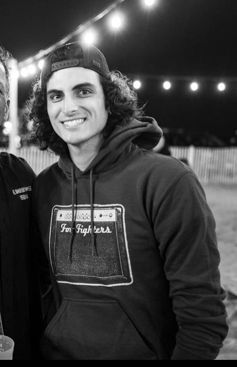 two men standing next to each other in front of some string lights and smiling at the camera