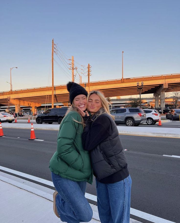 two women hugging each other in front of an overpass and traffic cones at sunset