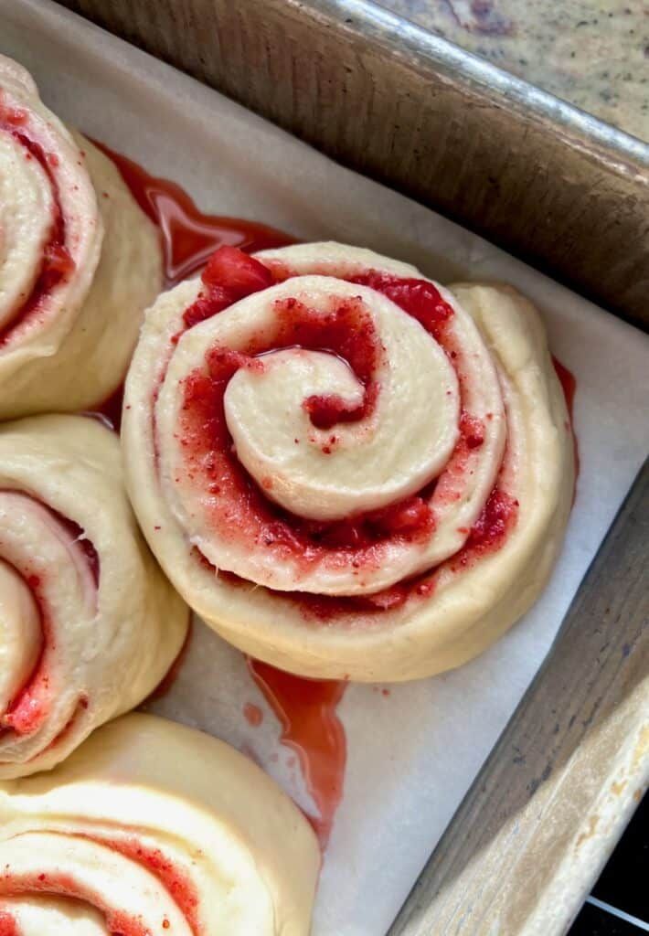 some very tasty looking pastries in a box with red stuff on them and sprinkled