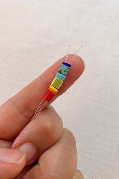 a person holding a tiny colorful object in their left hand and threading it together