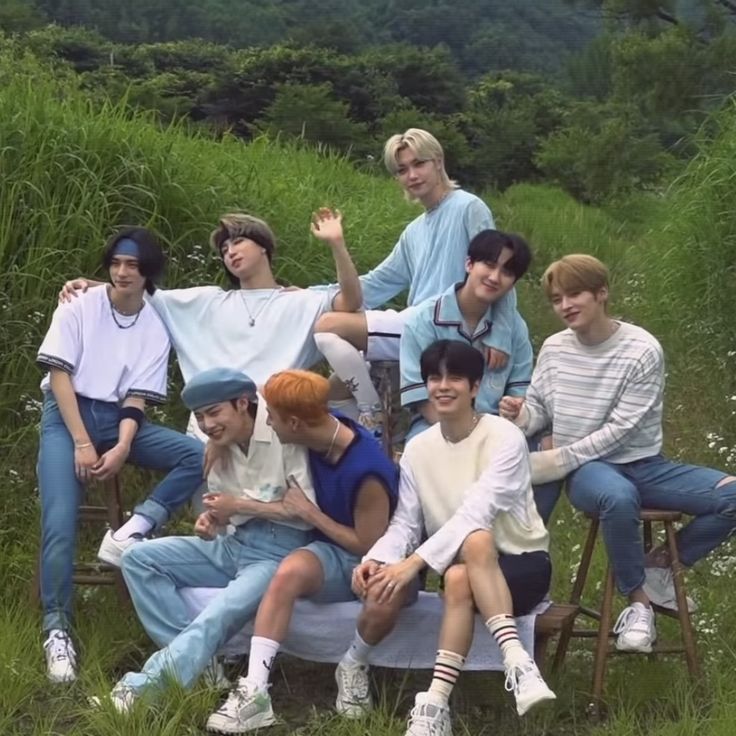 a group of young men sitting on top of a wooden bench next to tall grass