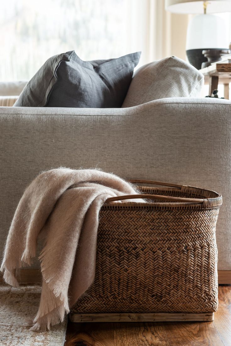 a basket sitting on the floor in front of a couch with pillows and throw blankets