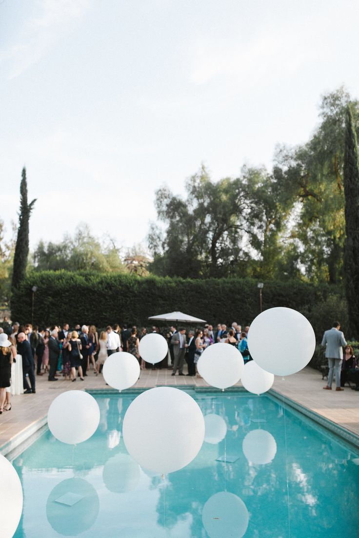 a group of people standing next to a pool filled with white balloons and confetti