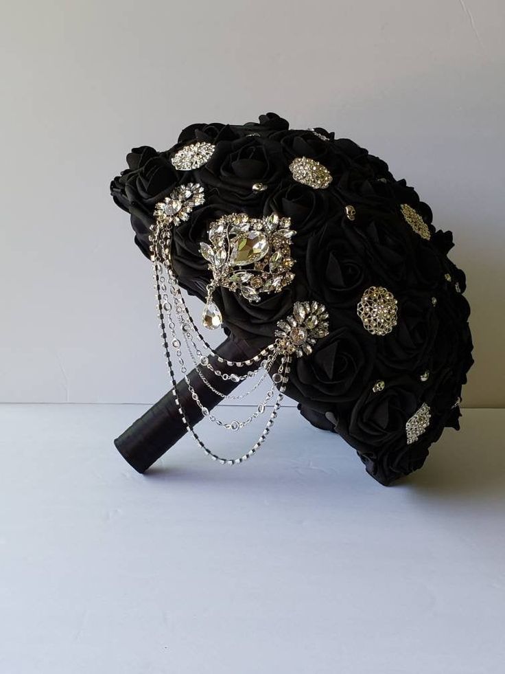 a bridal bouquet made with black roses and crystal brooches is displayed on a white surface