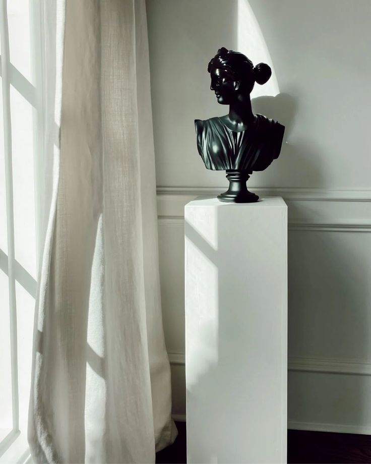 a black busturine sitting on top of a white pedestal next to a window