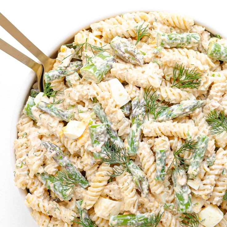 a white bowl filled with pasta salad topped with green onions and dill sprigs