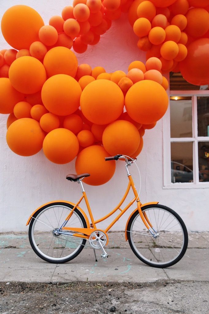 an orange bike parked in front of a building with balloons attached to the side of it