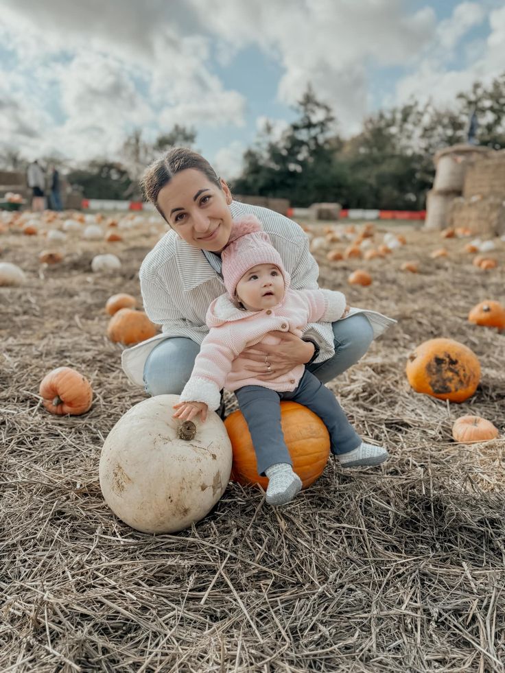 a woman holding a baby sitting on top of a pumpkin