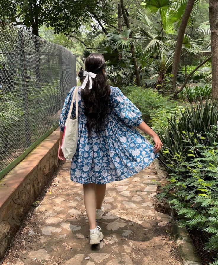 a woman in a blue dress walking down a path with her back to the camera