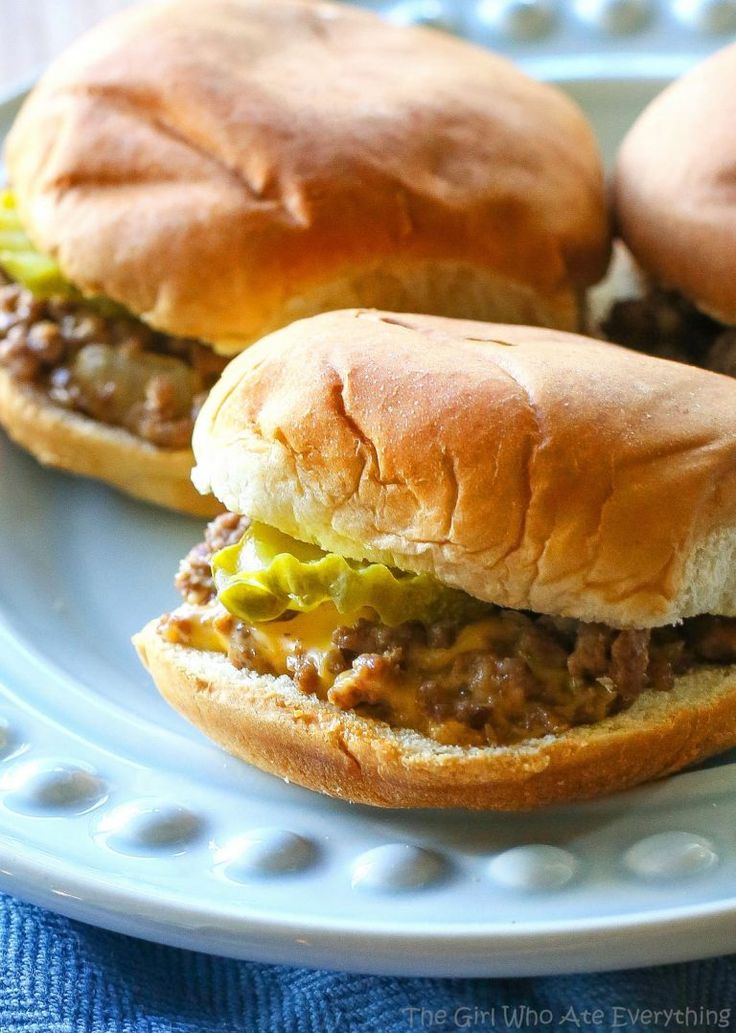 two sloppy joe sandwiches on a plate with a blue towel in the backgroud