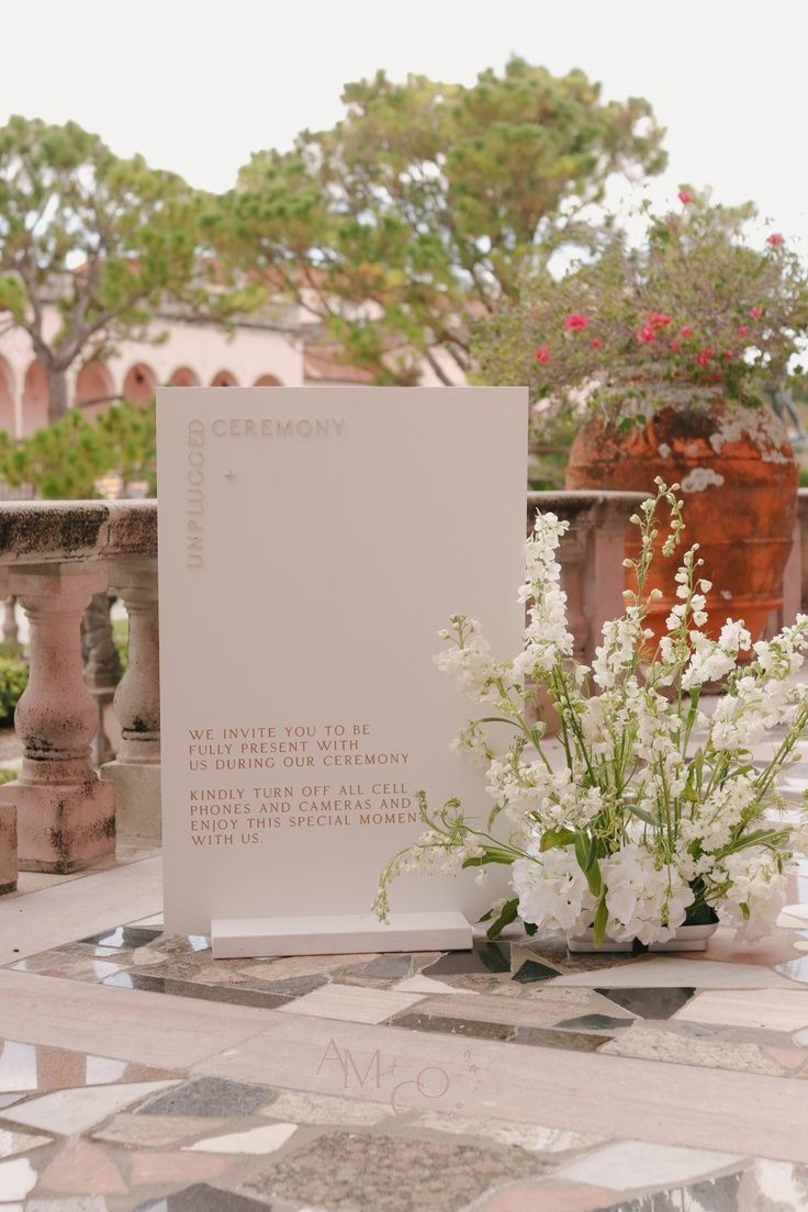 a vase with white flowers sitting on top of a tiled floor next to a sign