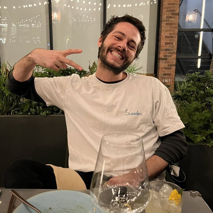 a man sitting at a table in front of a wine glass pointing to the side